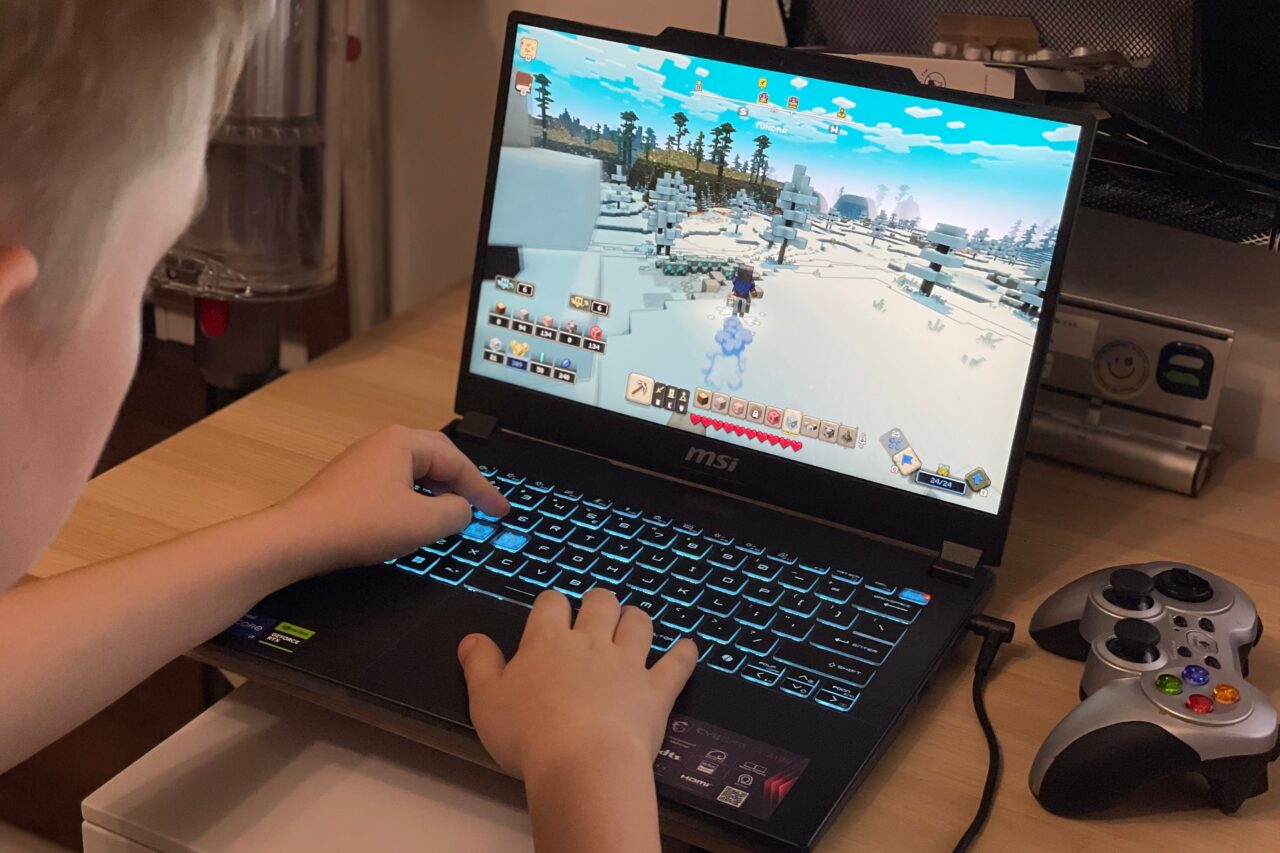 Dziecko grające na laptopie MSI w grę z widokiem z perspektywy trzeciej osoby w śnieżnym środowisku, obok kontroler do gier.