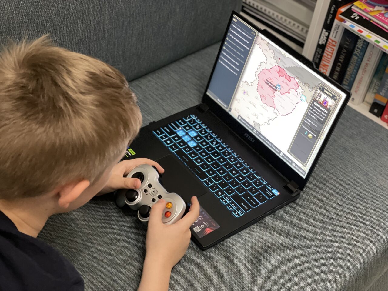 Chłopiec gra w grę strategiczną na laptopie przy użyciu kontrolera do gier.