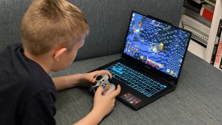 Chłopiec grający w grę komputerową na laptopie z podświetlaną klawiaturą, używając do tego gamepada.