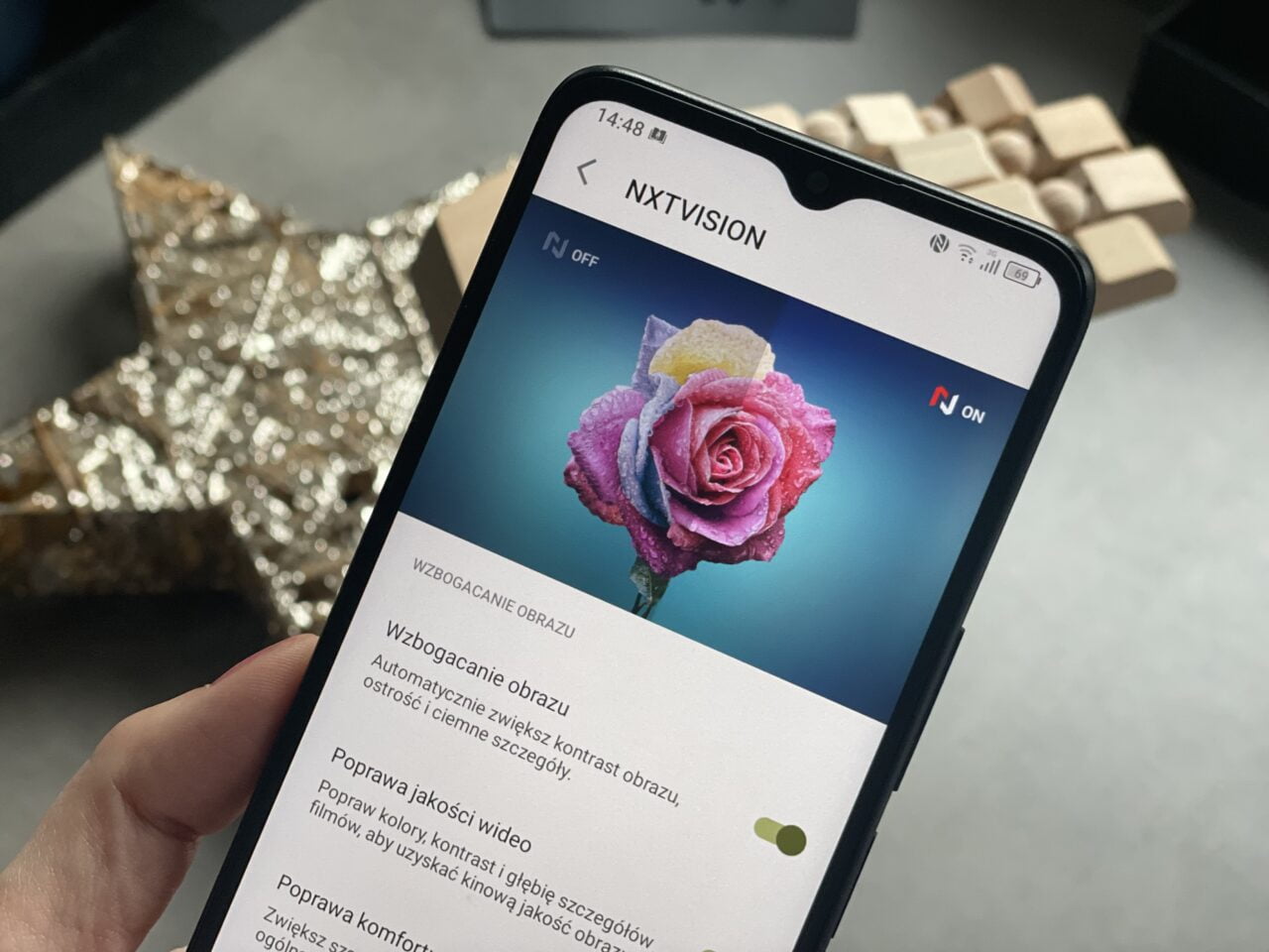 Ręka trzymająca smartfon z ekranem wyświetlającym różę w różnych kolorach, obok tekstu dotyczącego ustawień wzbogacania obrazu.