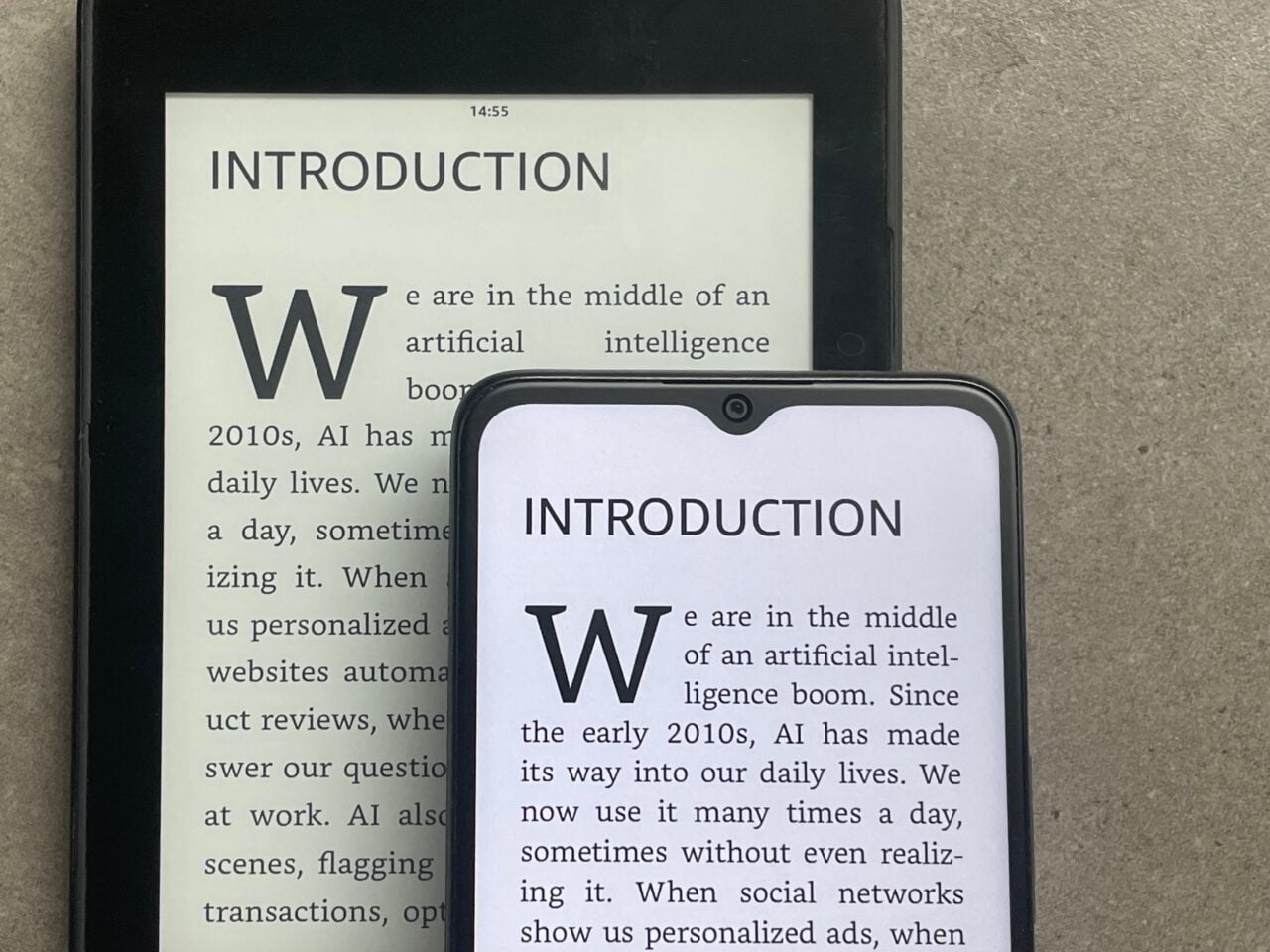 Czytnik e-booków i smartfon wyświetlające ten sam tekst z wstępu książki na temat sztucznej inteligencji, położone obok siebie na szarym tle.