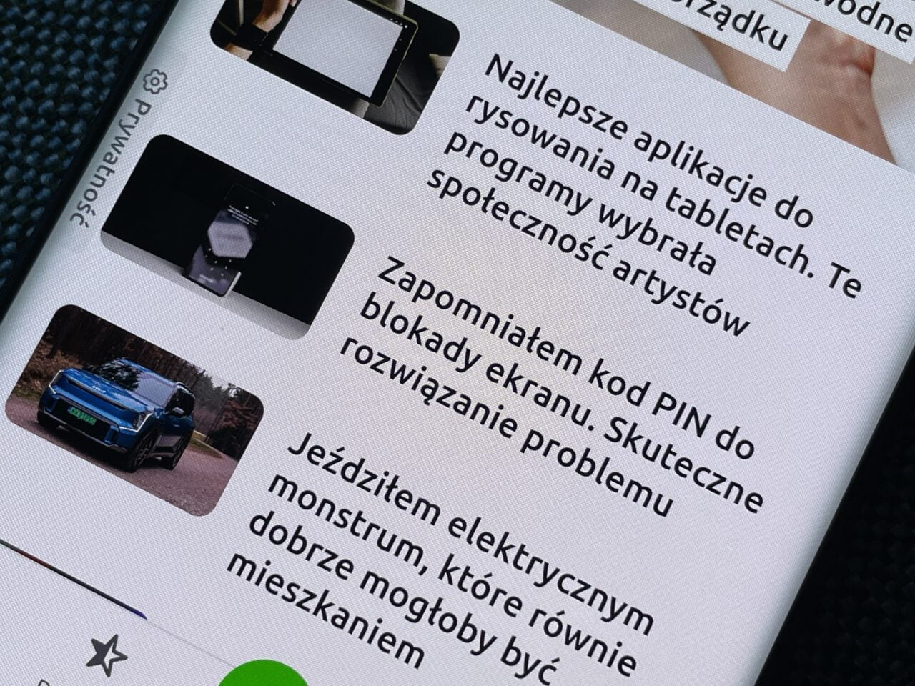 Ekran smartfona wyświetlający listę artykułów z miniaturkami, zawierający tekst w języku polskim oraz zdjęcie niebieskiego samochodu elektrycznego.