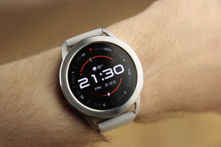 Zdjęcie wyróżniające w recenzji Xiaomi Watch S3, czyli zegarka widocznego na nadgarstku z wyświetlaczem pokazującym czas (21:30), datę (piątek, 23) oraz różne wskaźniki, jak tętno, kroki, spalone kalorie i temperaturę.