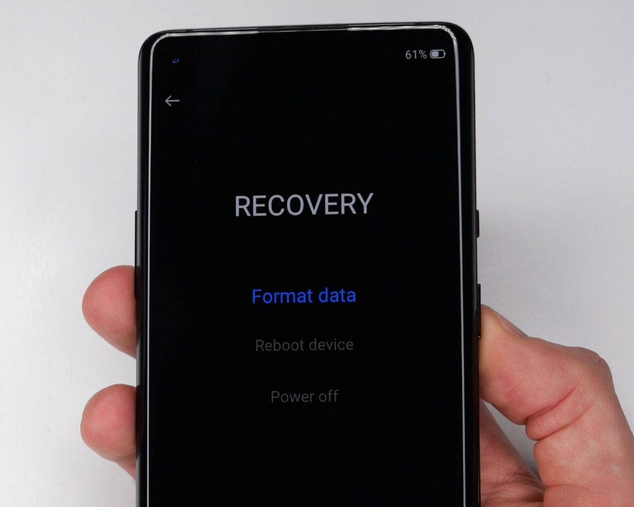Dłoń trzymająca smartfon wyświetlający menu odzyskiwania z opcjami "Format data", "Reboot device" i "Power off".