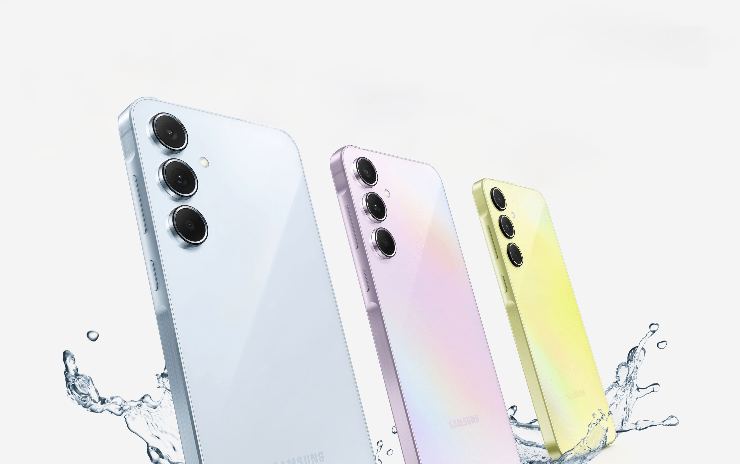 Trzy smartfony Samsunga różnych kolorów, umieszczone pionowo z aparatem skierowanym na widz, na białym tle z efektem rozbryzgującej się wody.