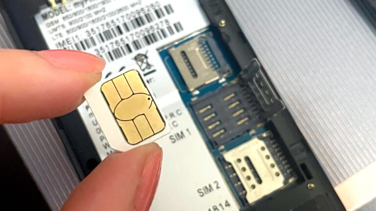 Ręka trzymająca kartę SIM nad otwartym gniazdem SIM w smartfonie.