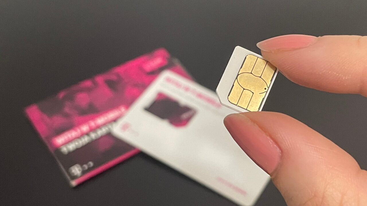 Osoba trzyma kartę SIM pomiędzy palcami, w tle opakowanie karty SIM.