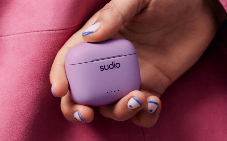 Etui ładujące do słuchawki Sudio w kolorze fioletowym trzymane w dłoni z pomalowanymi paznokciami w białym i niebieskim kolorze.