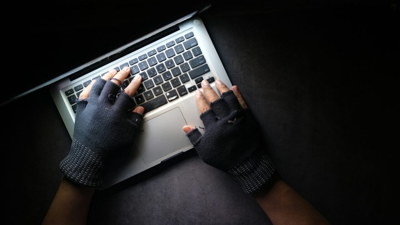 Ręce w bezpalczatkach piszące na laptopie na ciemnym tle.