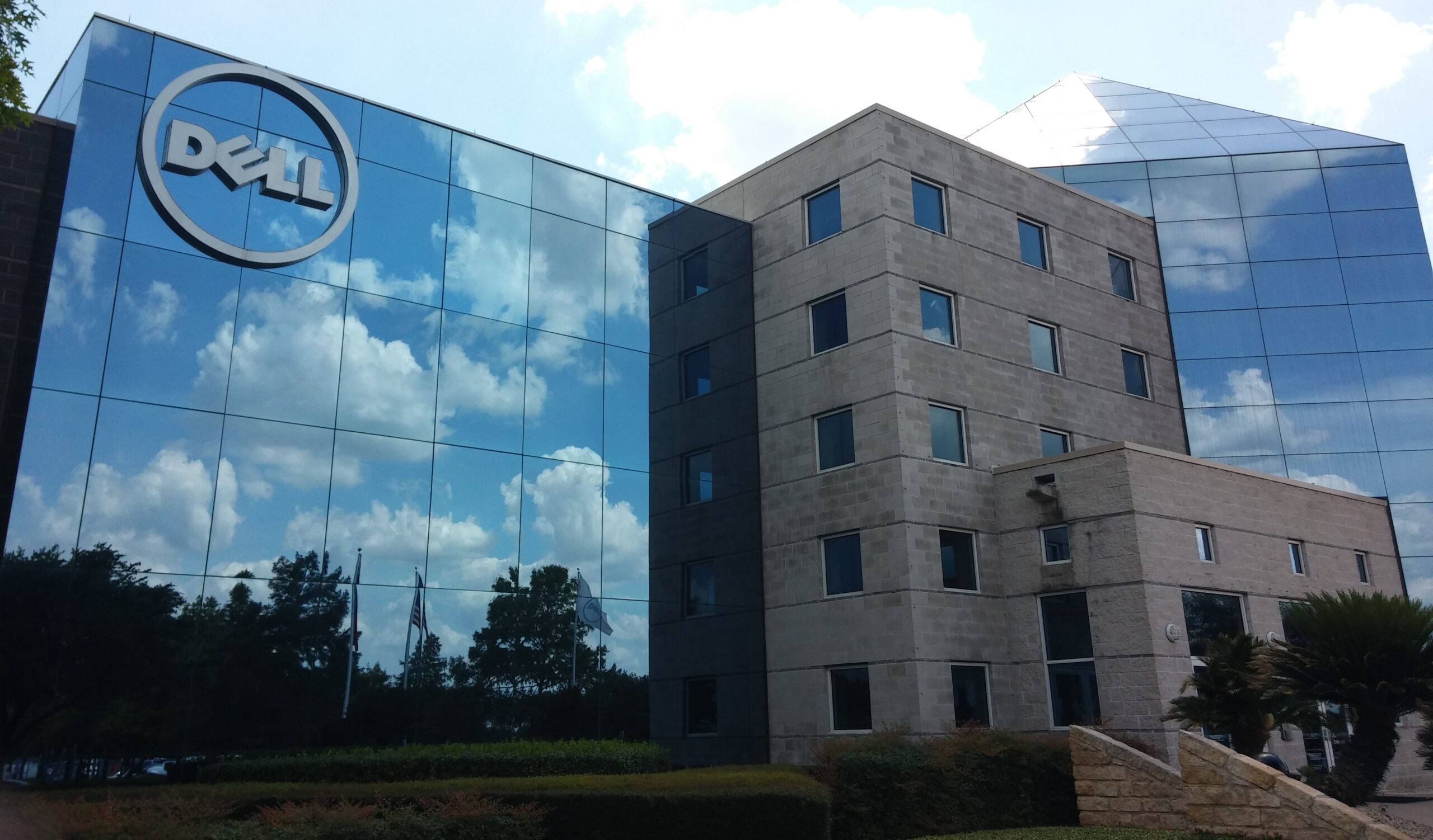 Zdjęcie nowoczesnego biurowca z dużym logo firmy Dell na szklanej fasadzie, odbijającym błękitne niebo i chmury. Ultimatum DELL dla pracowników jest jasne