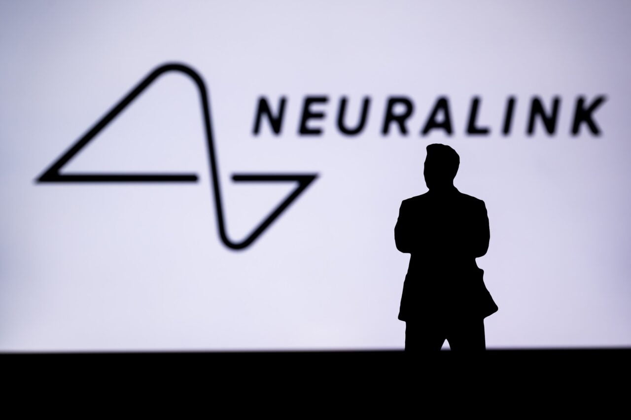 Pierwszy pacjent neuralink. Silna sylwetka osoby stojącej przed projekcją z logo "Neuralink".