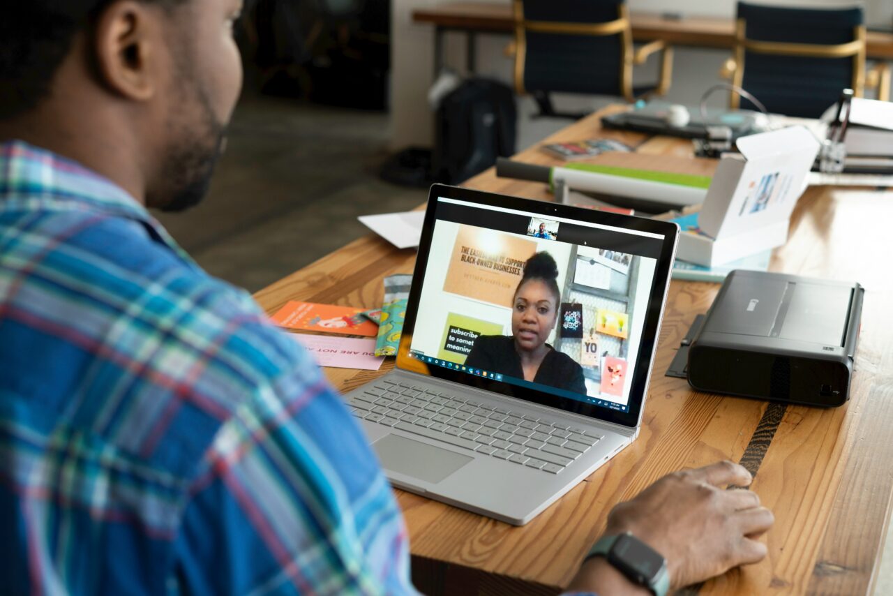 Mężczyzna uczestniczący w wideokonferencji na laptopie w biurze. Na ekranie laptopa widoczna jest kobieta mówiąca na wideokonferencji.