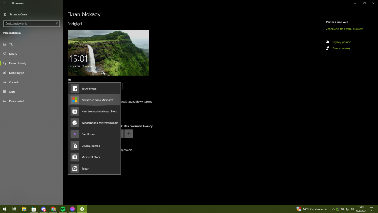 Zrzut ekranu interfejsu użytkownika Windows z otwartym menu Ustawienia i zaakcentowaną sekcją personalizacji, ekranu blokady z podglądem pokazującym krajobraz z wodospadem i zielonym wzgórzem. W prawym górnym rogu znajduje się zegar i data.