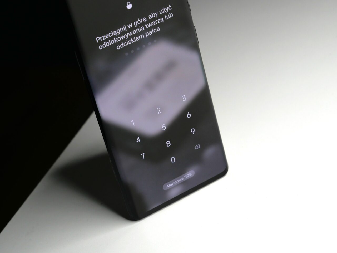Smartfon leży na białym stole z widocznym ekranem blokady i klawiaturą numeryczną do wprowadzania kodu PIN.