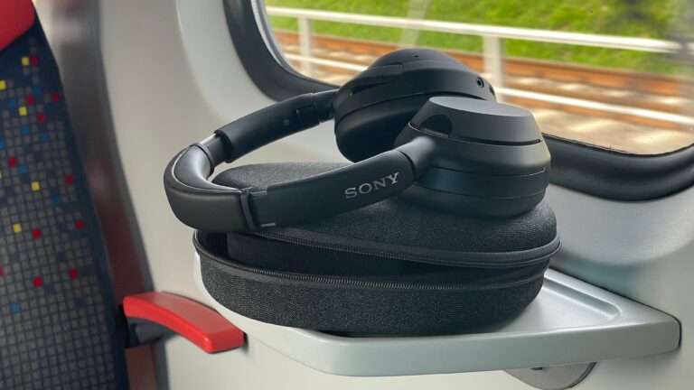 Czarne słuchawki nauszne marki Sony leżące na twardym etui, umieszczone na składanym stoliku w wagonie pociągu.
