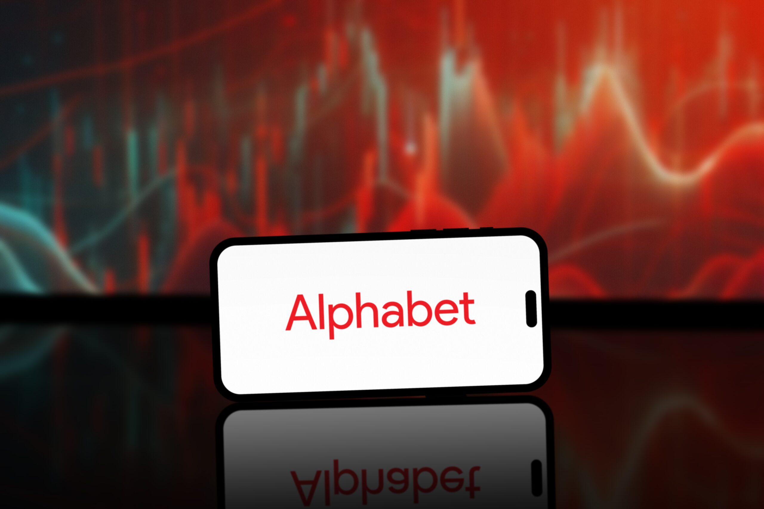 Smartfon z napisem "Alphabet" na ekranie, na tle czerwono-czarnych abstrakcyjnych wzorów.