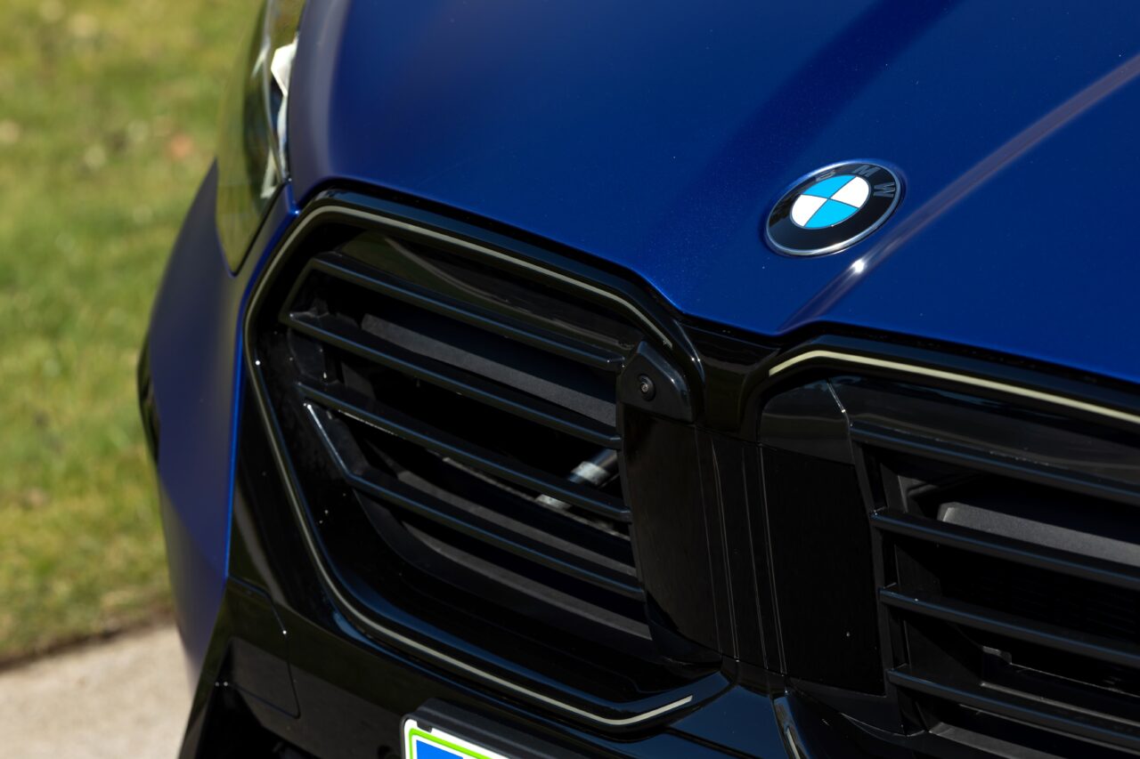 Przód samochodu marki BMW z wyraźnym logo na niebieskiej masce i szczegółami przedniego grilla.