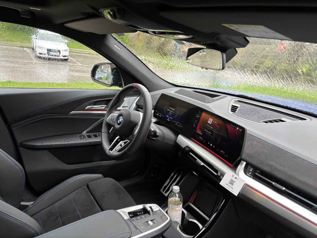 Wnętrze samochodu BMW z czarnymi skórzanymi siedzeniami, kierownicą z logotypem marki, cyfrowymi zegarami i ekranem dotykowym w centralnej części deski rozdzielczej.
