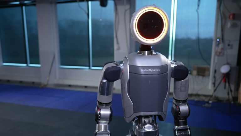 Robot humanoidalny Boston Dynamics stojący w pomieszczeniu z oknami w tle.