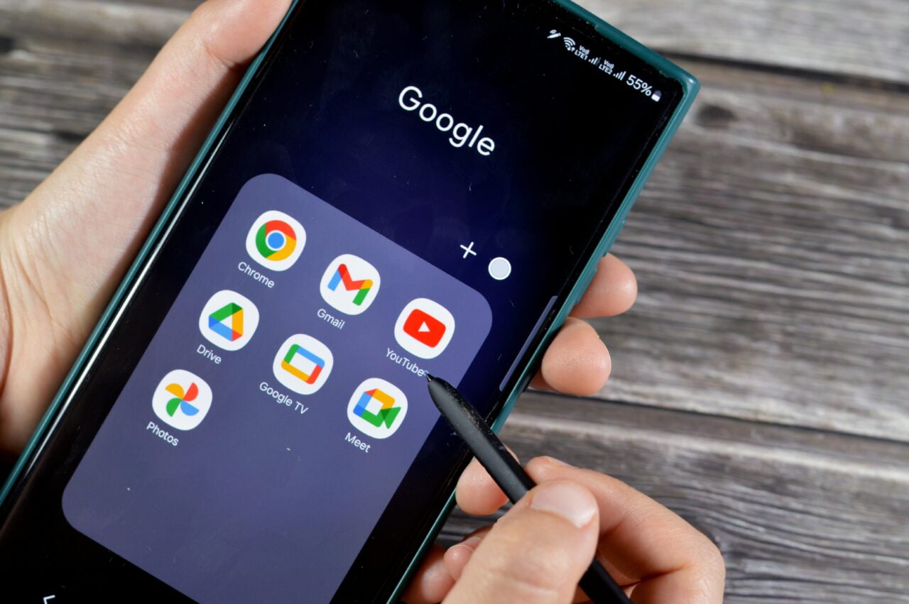 Ręka trzymająca smartfon z otwartą aplikacją Google i ikonami różnych aplikacji Google takimi jak Chrome, Gmail, YouTube na ekranie.