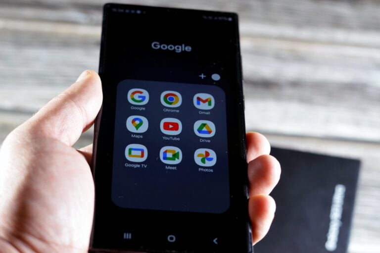 Dłoń trzymająca smartfon z ekranem, na którym wyświetla się grupa aplikacji Google.
