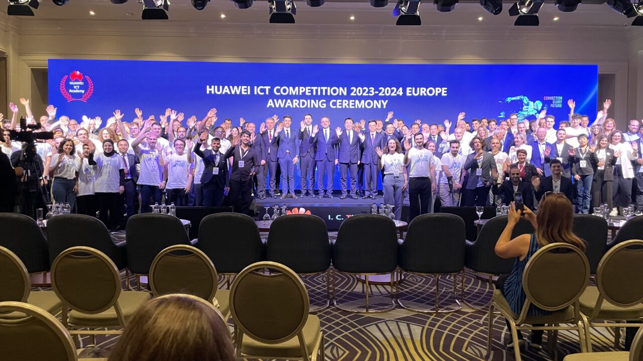 Huawei ICT Competition Europe. Duża grupa ludzi pozuje na zdjęciu na scenie podczas ceremonii wręczenia nagród Huawei ICT Competition 2023-2024 w Europie.