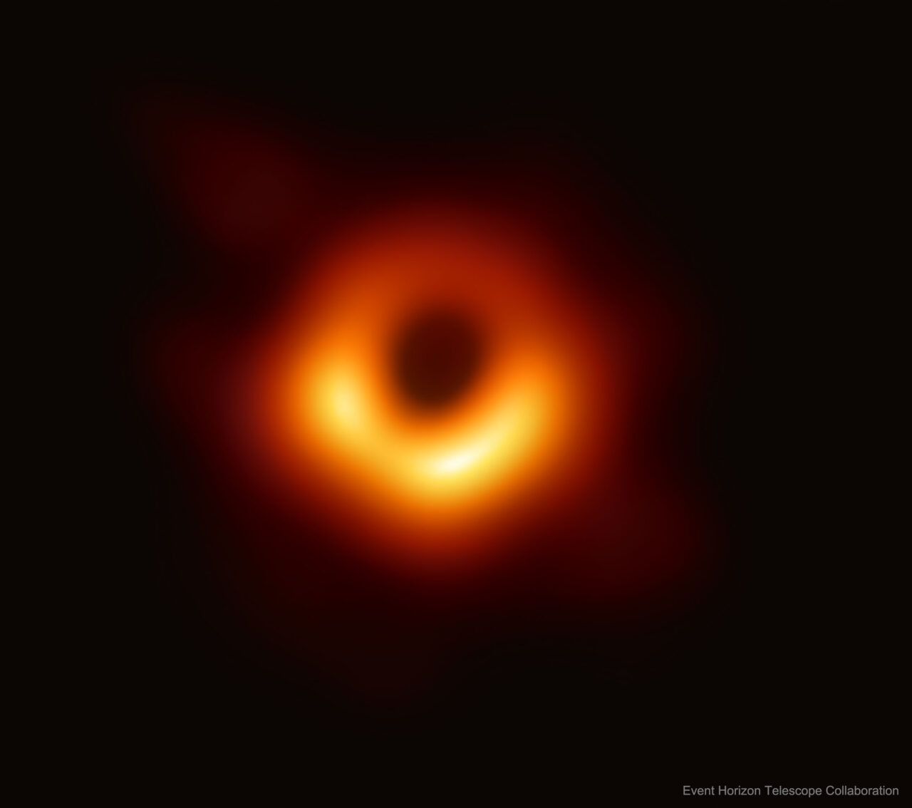 Zdjęcie pierwszego sfotografowanego czarnej dziury, jasne żółte światło koncentruje się wokół ciemnego centralnego punktu na tle rozmytych czerwono-pomarańczowych tonów.