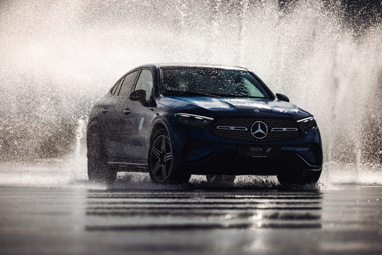Niebieski samochód Mercedes-Benz przejeżdżający przez wodę na drodze, tworzący efektowny rozbryzg wokół pojazdu.