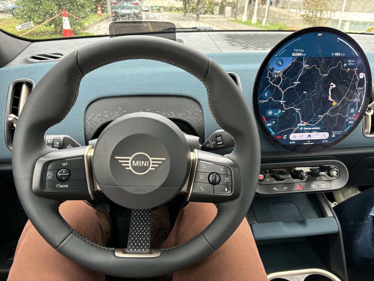 Wnętrze pojazdu marki MINI z widokiem na kierownicę i cyfrowy ekran nawigacji satelitarnej po prawej stronie.