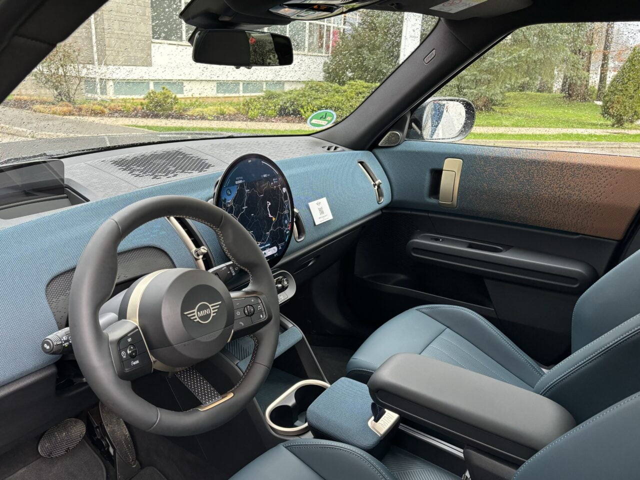 Wnętrze nowoczesnego samochodu z widokiem na kierownicę, deski rozdzielczej, wyświetlacz nawigacyjny i część przednich foteli, wykonane z materiałów w odcieniach szarości i niebieskiego.