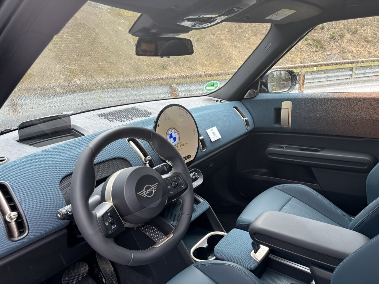 Wnętrze samochodu osobowego z widoczną kierownicą z emblematem Mini, niebieskimi fotelami, deska rozdzielcza z wyświetlaczem i niebieskie elementy wykończenia.