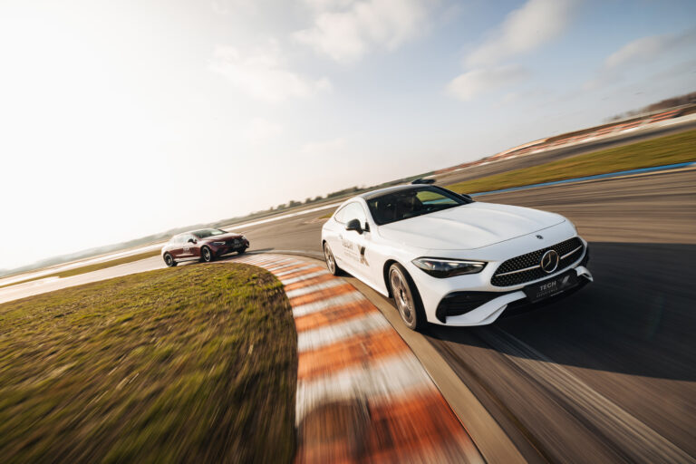 Dwa samochody sportowe, jeden biały a drugi burgundowy, jadą szybko na torze wyścigowym.
