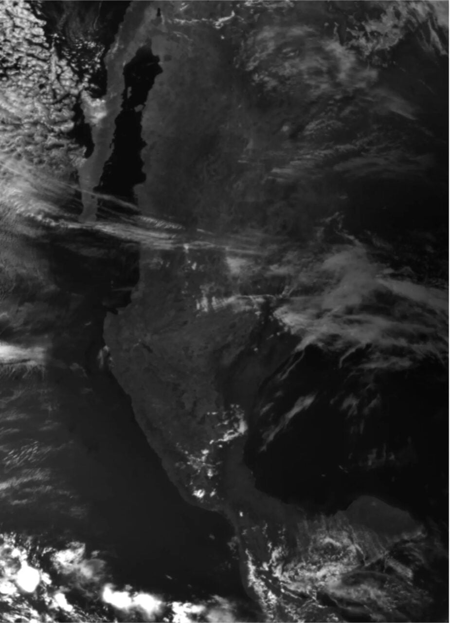 Satelitarny obraz w skali szarości przedstawiający kontur kontynentu afrykańskiego z widocznymi chmurami.