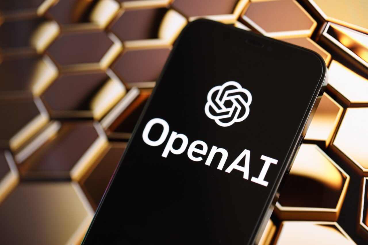 Smartfon z logo OpenAI (chatgpt) na ekranie, na tle złotych heksagonalnych struktur.
