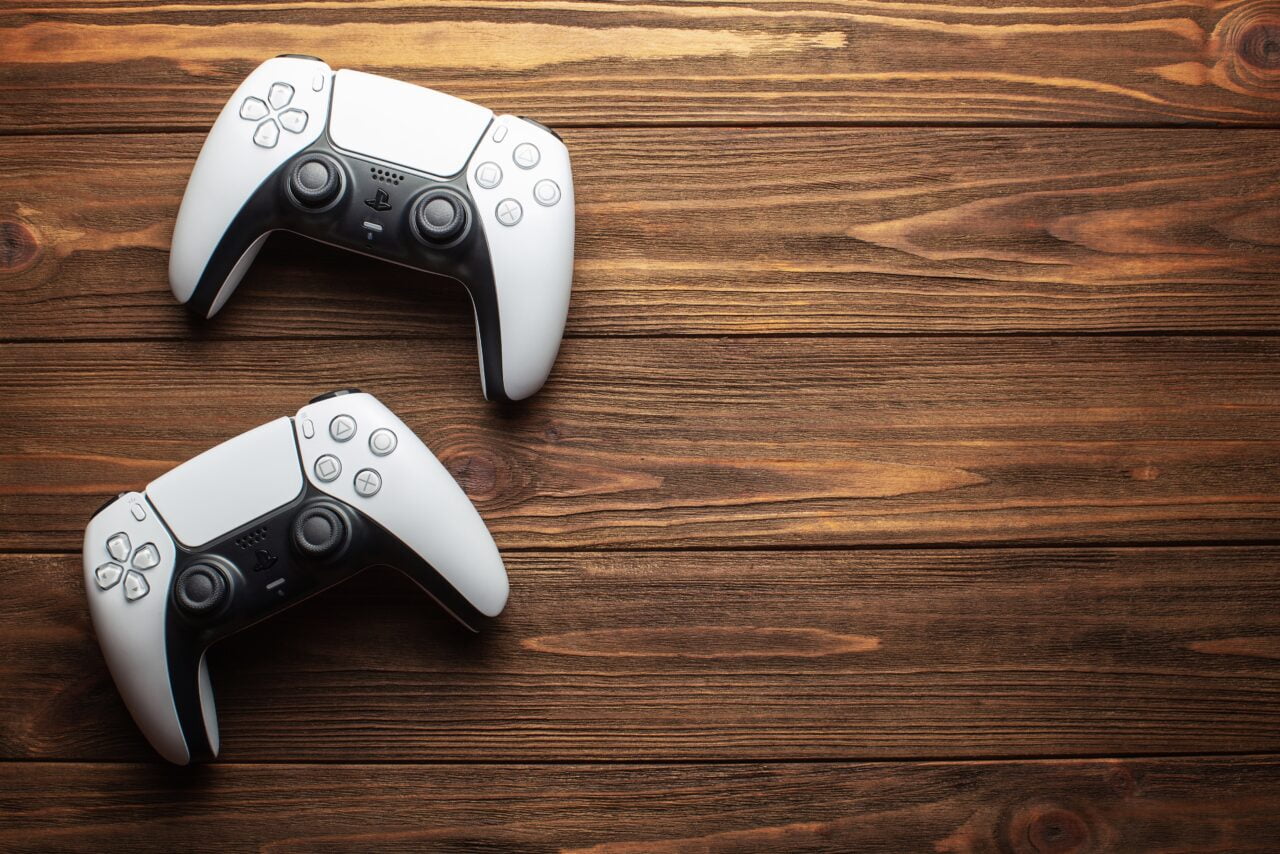 Dwa białe kontrolery DualSense do PlayStation 5 na drewnianym tle. Zdjęcie do tekstu pt. sprzedaż PlayStation 5 jako ilustracja
