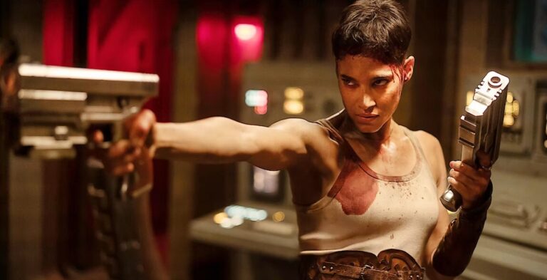 Kadr z filmu Rebel Moon. Kobieta trzymająca broń w pozycji bojowej, z krwawym śladem na twarzy, w science-fiction otoczeniu.