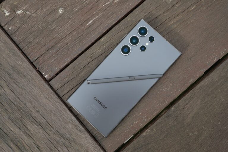 Smartfon Samsung leżący ekranem do dołu na drewnianym podłożu, z rysikiem umieszczonym na jego tylnej części.