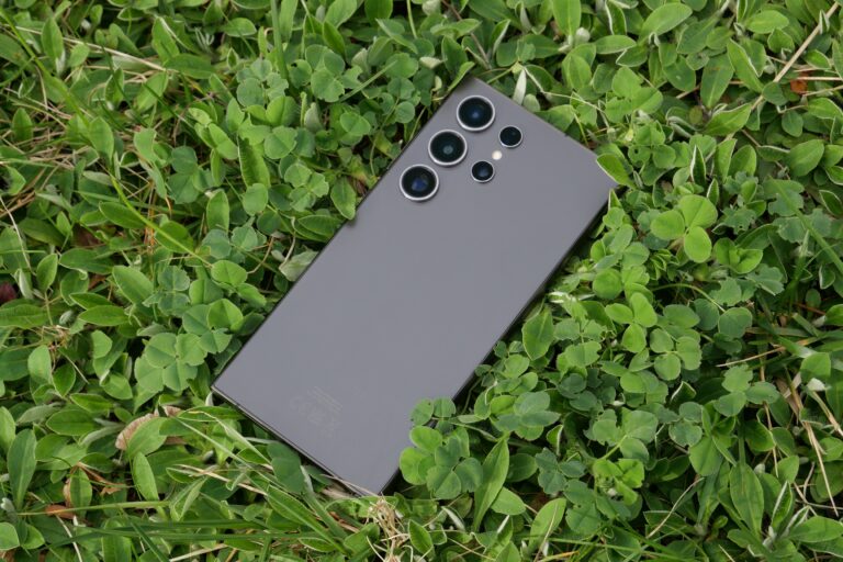 Czarny smartfon z potrójnym aparatem umieszczony na zielonej trawie z koniczyną, dostępny w sieci Komputronik.