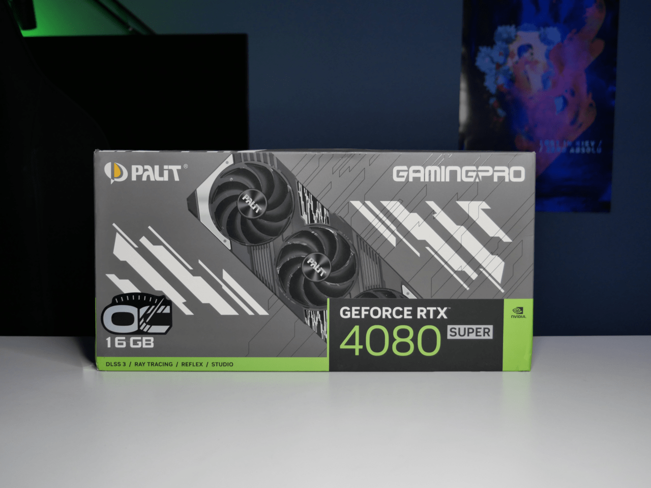 Opakowanie karty graficznej Palit GamingPro GeForce RTX 4080 SUPER z logo Nvidia, znajdujące się na biurku z podświetleniem LED na tle monitora komputerowego i plakatu.