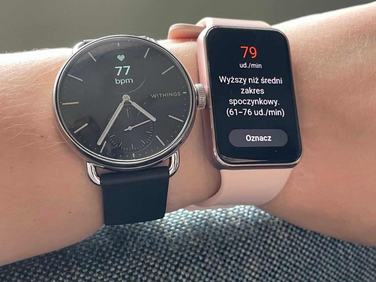 Dwa smartwatche na nadgarstku: zegarek Withings pokazujący tętno 77 bpm i smartwatch w różowej obudowie z ekranem pokazującym tętno 79 uderzeń na minutę i napis "Wyższy niż średni zakres spoczynkowy".