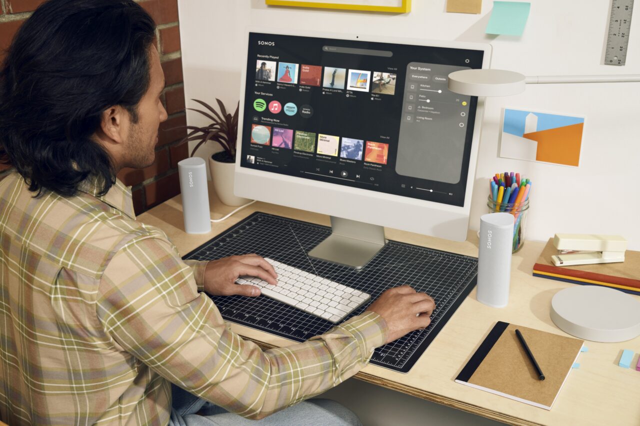 Mężczyzna siedzący przy biurku w kreatywnym biurze korzysta z komputera, na ekranie wyświetlacz multimedialny Sonos.