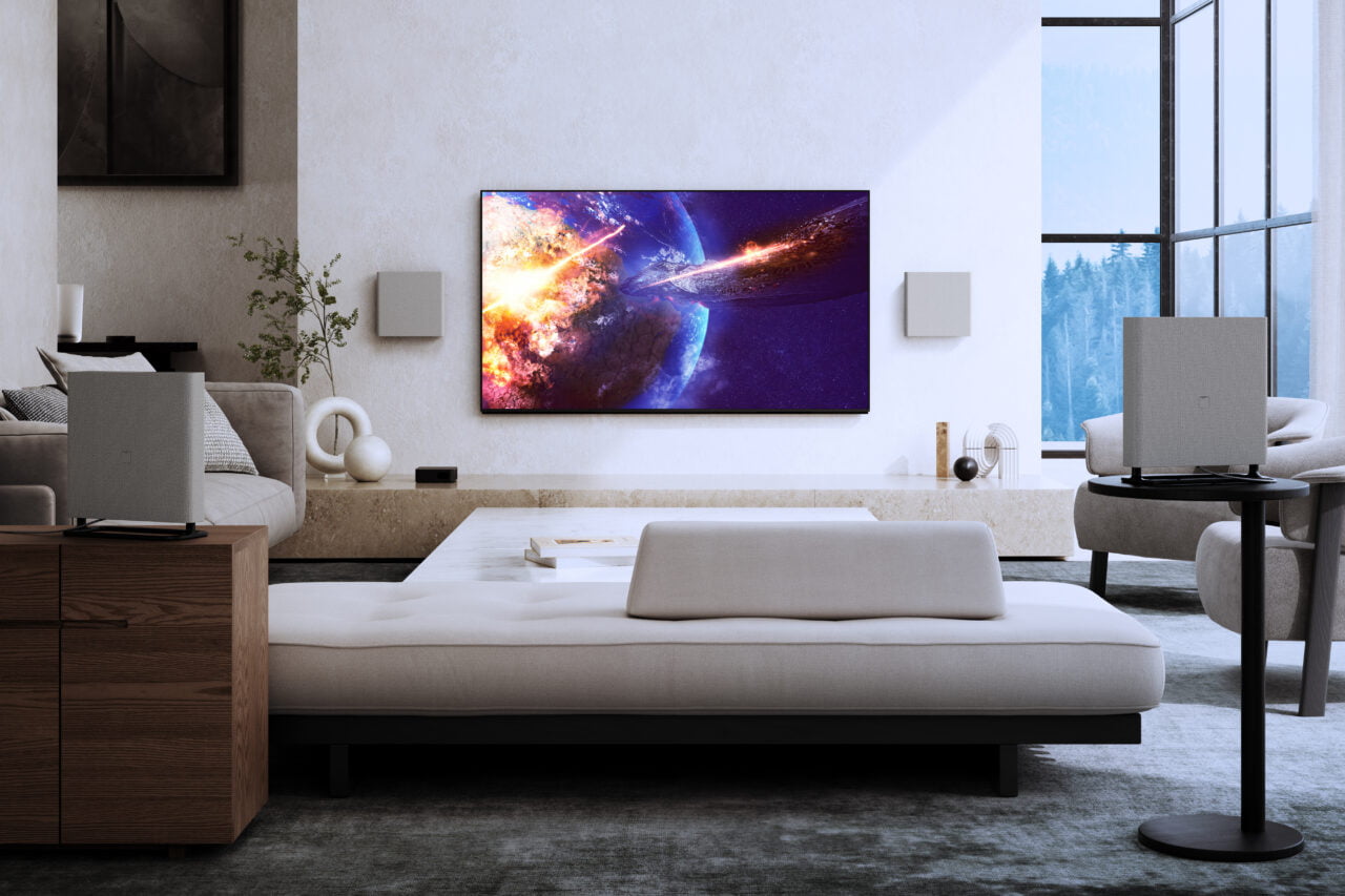 Nowe telewizory Sony BRAVIA. Nowoczesny salon z dużym telewizorem zawieszonym na ścianie wyświetlającym obraz kosmosu, sofą, fotelami i dużym oknem z widokiem na las.