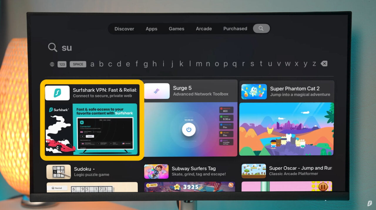 Surfshark VPN dla Apple TV. Wyświetlacz komputera z otwartym sklepem aplikacji pokazujący różne aplikacje i gry na kolorowym tle z pomarańczową lampą.