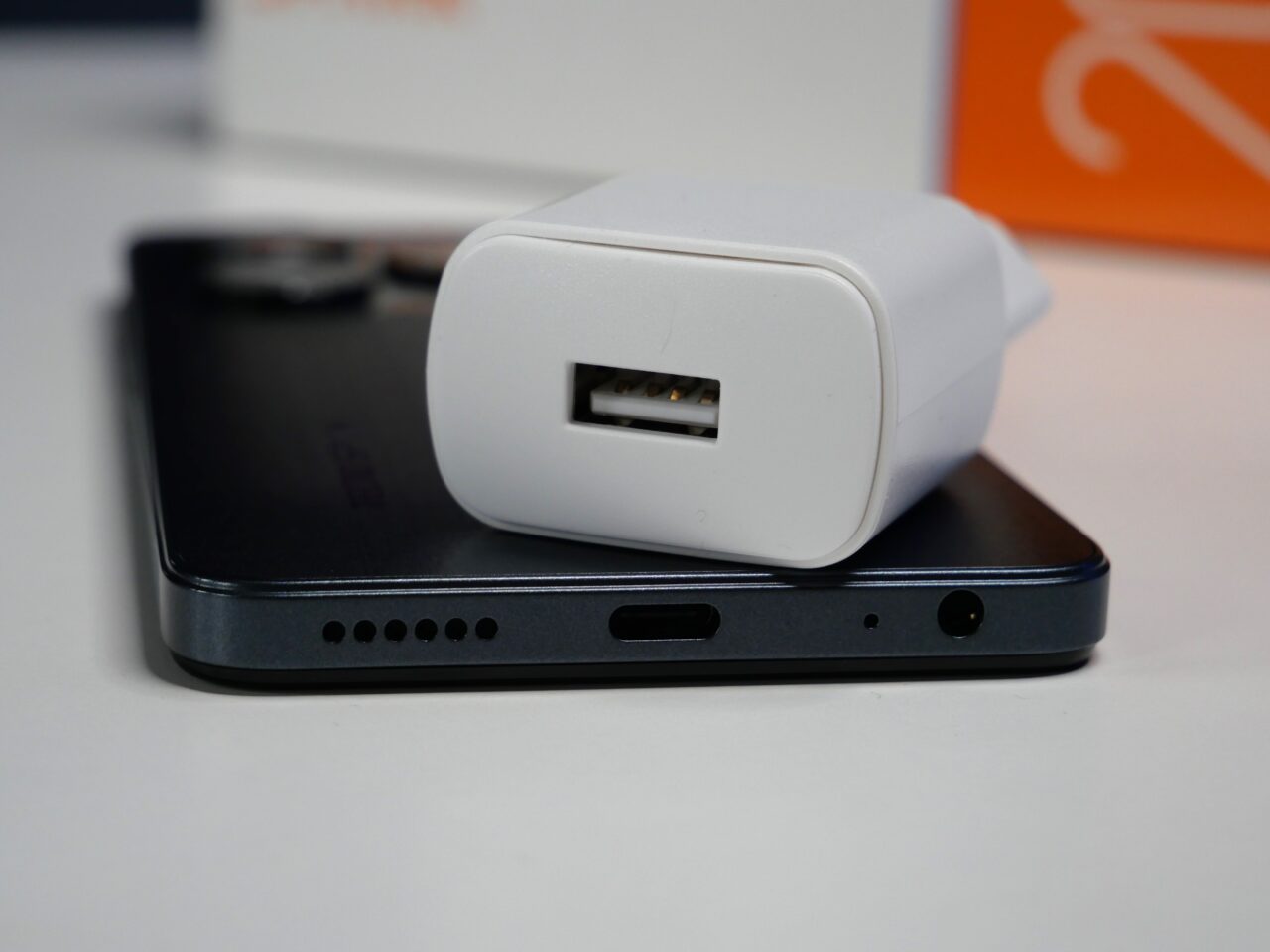 Ładowarka USB leżąca na czarnym smartfonie na białym tle.