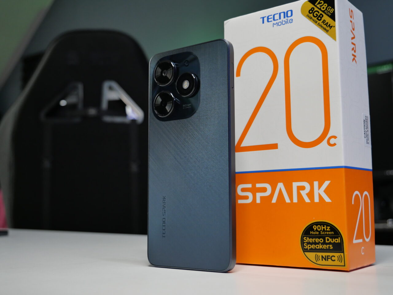 Smartfon Tecno Spark 20 w kolorze niebieskim z tyłu obok pudełka z napisem "SPARK 20".