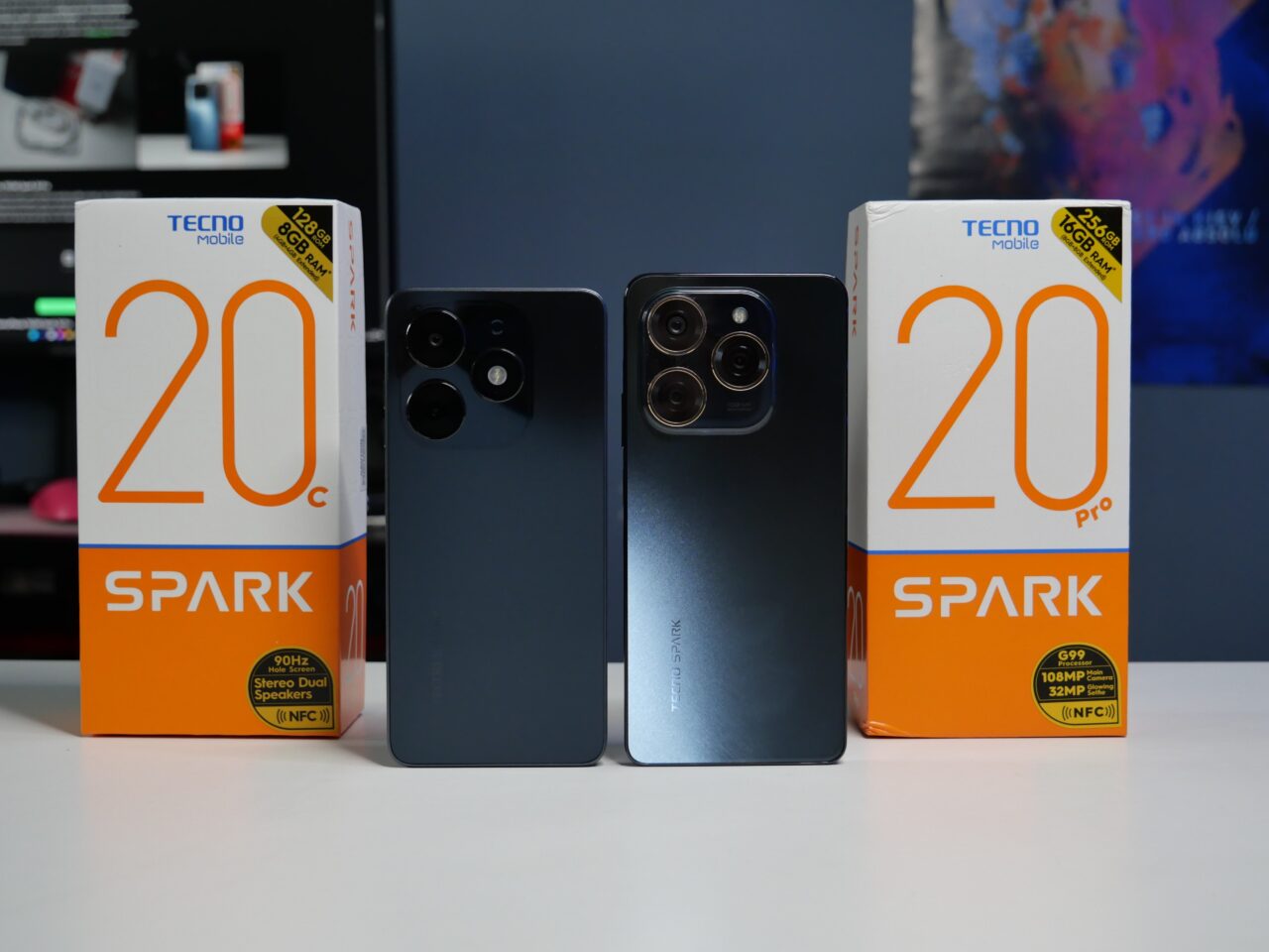 Dwa smartfony Tecno Spark 20C i 20 Pro stojące obok swoich pudełek na biurku.