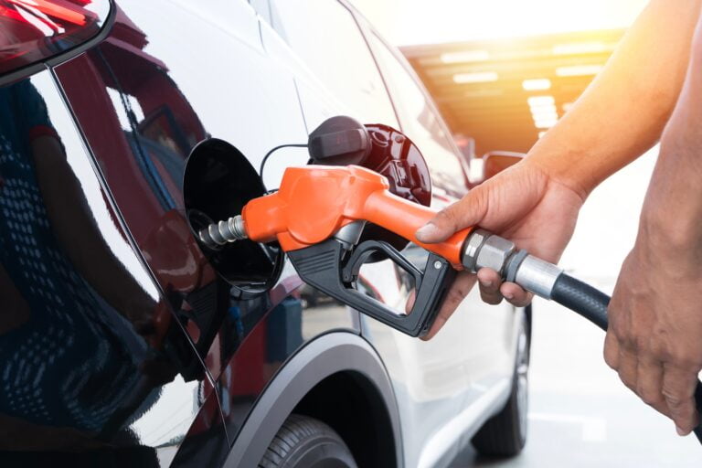 Tankowanie czerwonego samochodu na stacji benzynowej, ręka trzyma pomarańczową dyszę paliwową.