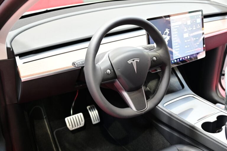 Wnętrze samochodu Tesla z kierownicą, wyświetlaczem i elementami drewnianymi na desce rozdzielczej.