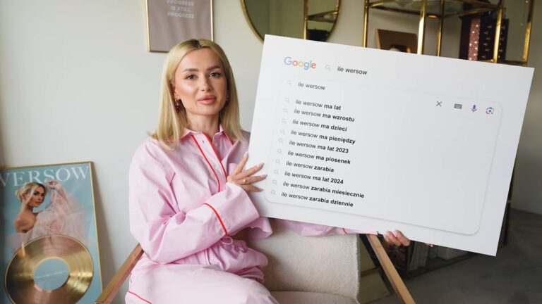 Kobieta w różowym kostiumie trzyma duży model ekranu wyszukiwarki Google z autokompletowaniem zapytań na temat "ile wersow". Obok niej złota płyta i magazyn z jej zdjęciem na okładce.