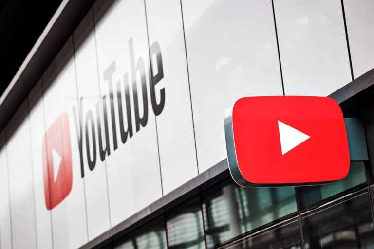 Logo YouTube na czerwonym prostokącie zamontowane na szklanej fasadzie budynku z napisem YouTube w tle.